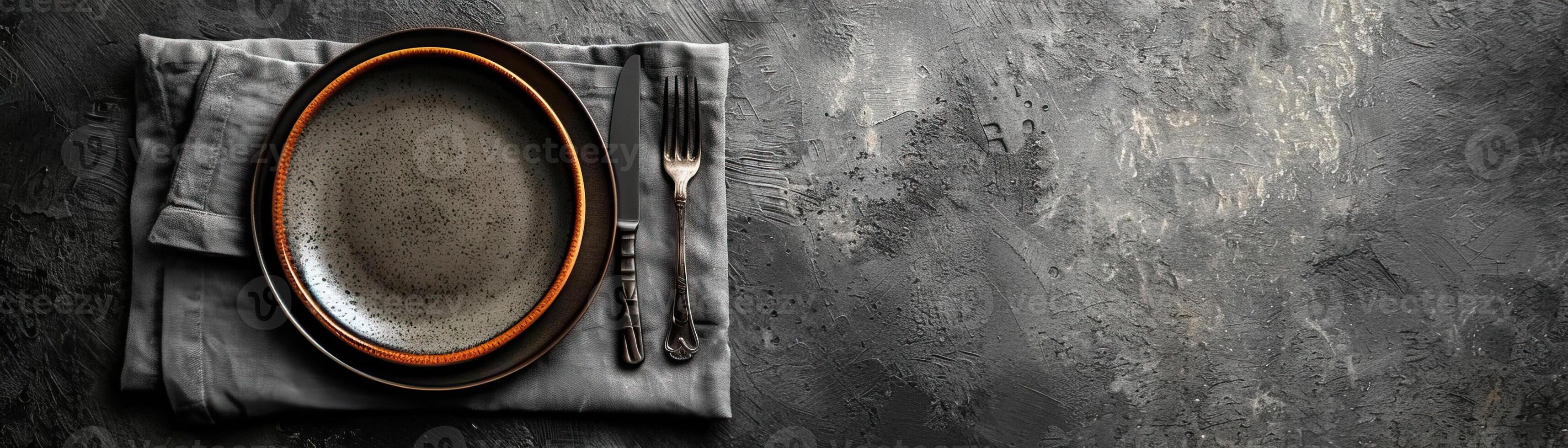 A contemporary, clean setup with a plate, knife, and fork on a minimalist grey napkin, set against a sleek, grey background, wide space above for editorial content. photo