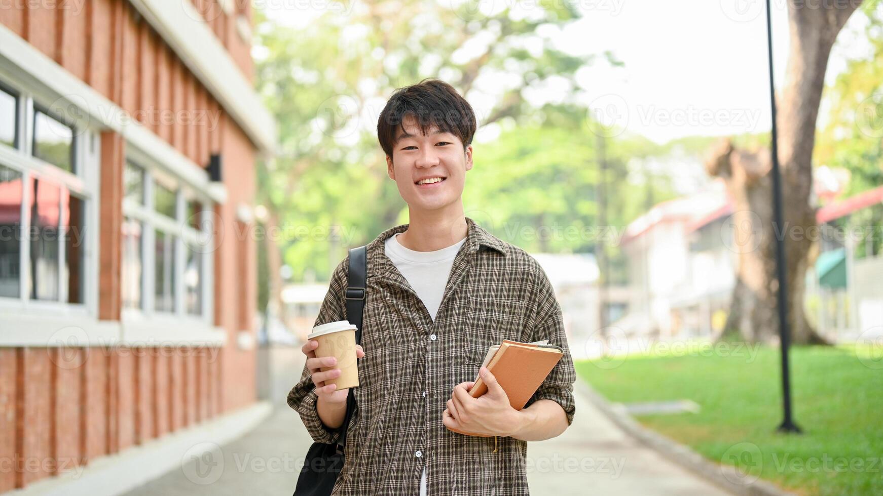 A young man college student, carrying a backpack, stands in front of a brick building on campus. photo