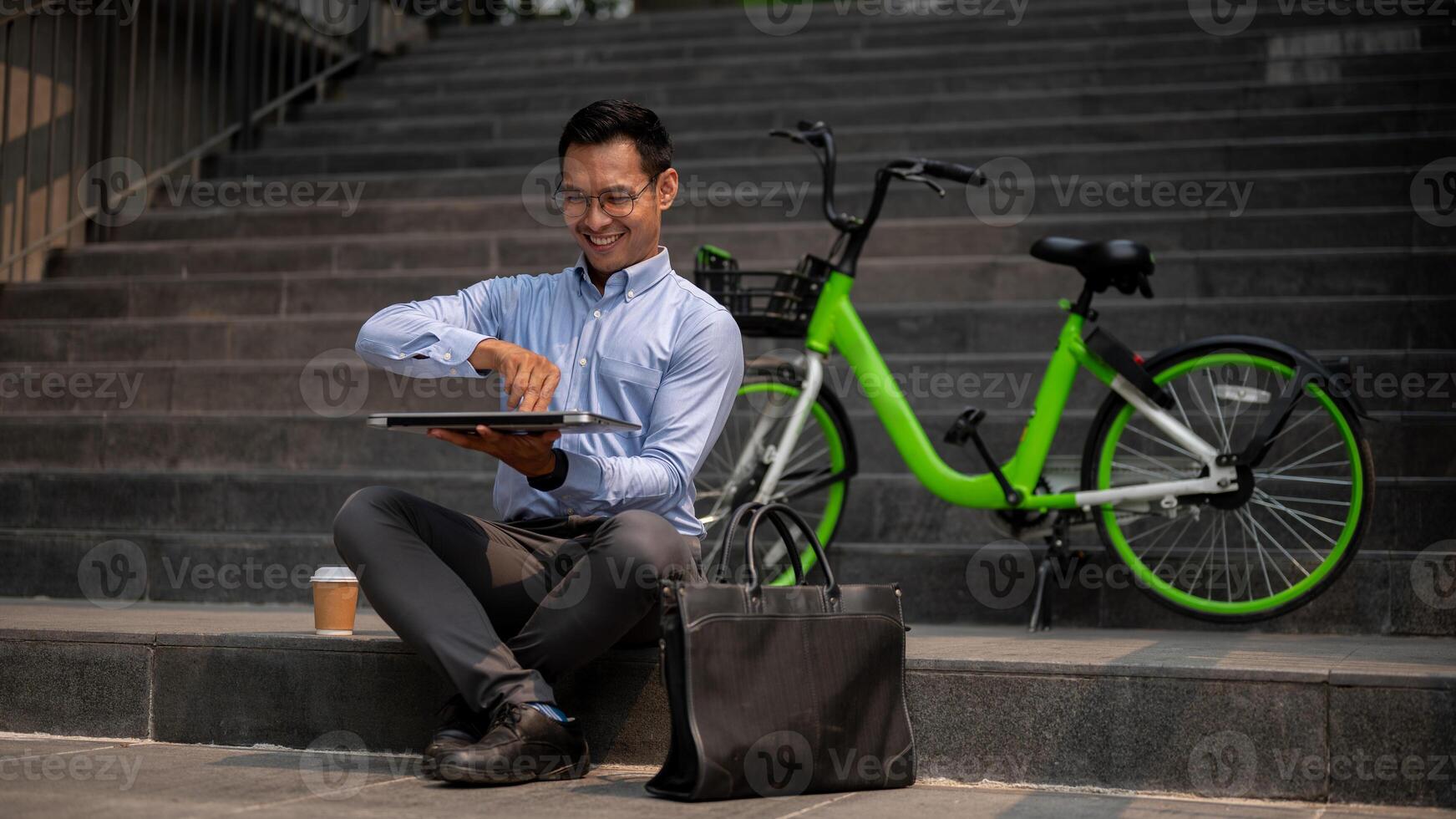 An Asian businessman sits on outdoor steps, opening his laptop, working remotely outdoors. photo