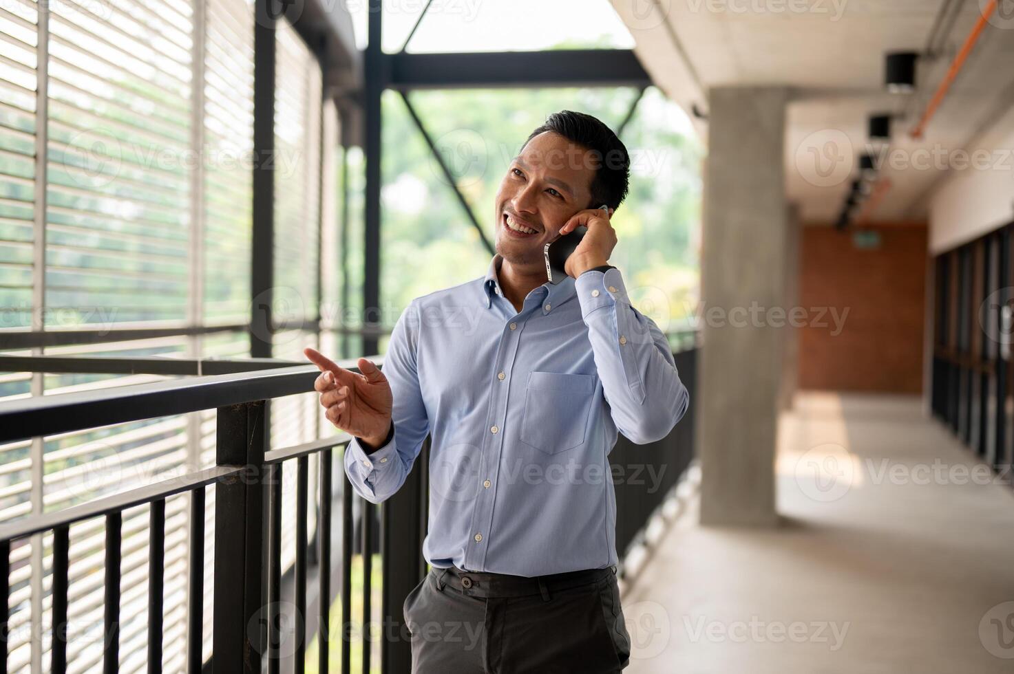 A confident Asian businessman talking on the phone with his client while walking on a corridor. photo