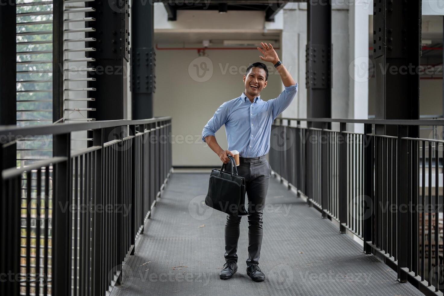 A friendly Asian businessman waving to greet his colleague while walking along the building corridor photo