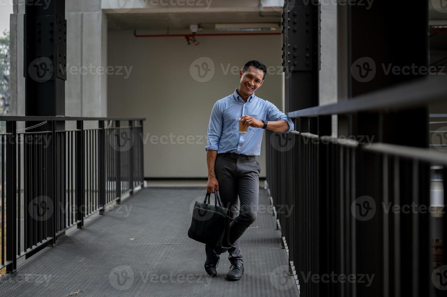 A handsome Asian businessman standing in the building corridor, taking a coffee break outdoors. photo