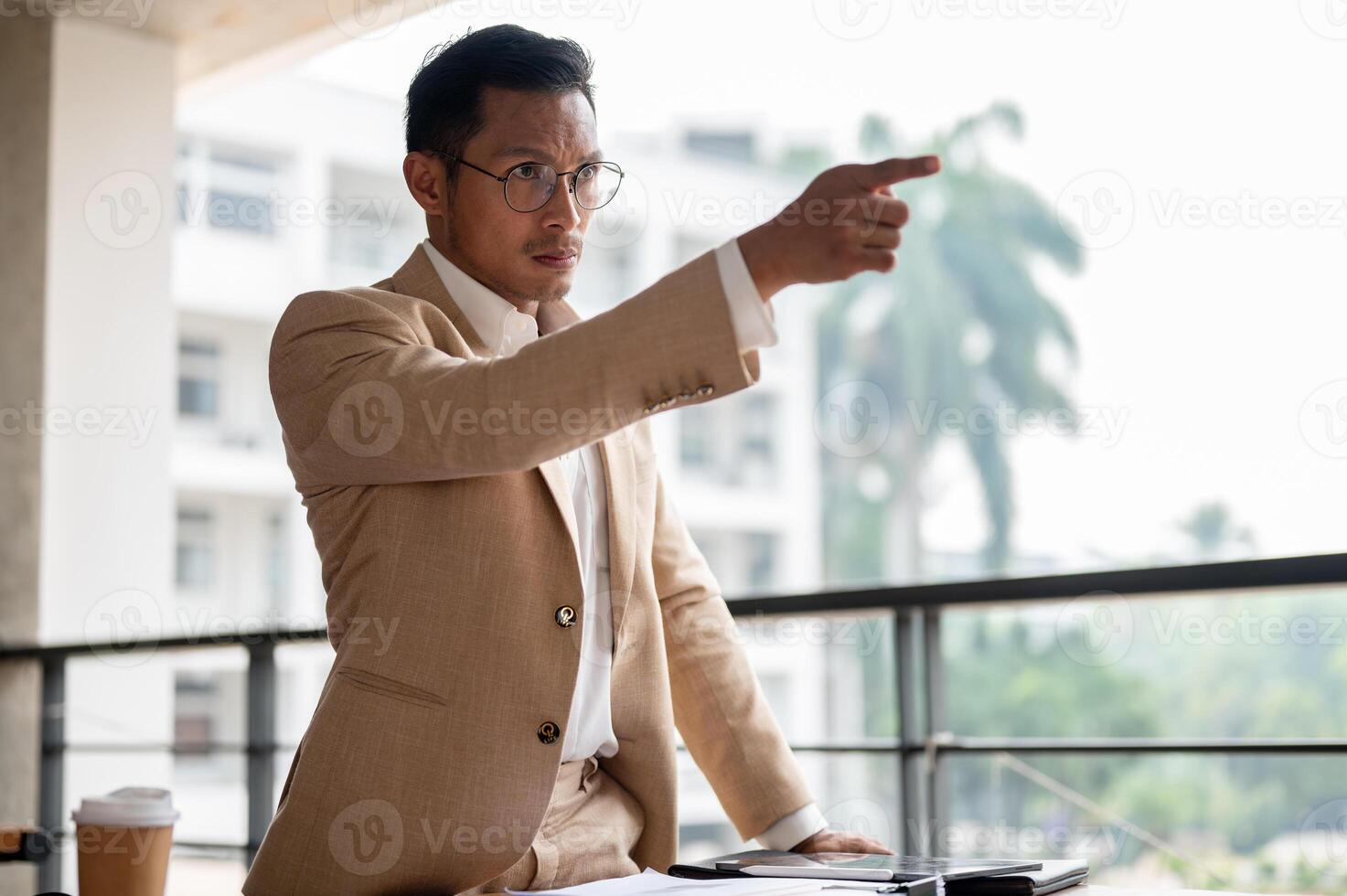 An angry Asian businessman is pointing his finger with angry expression, standing at a table. photo