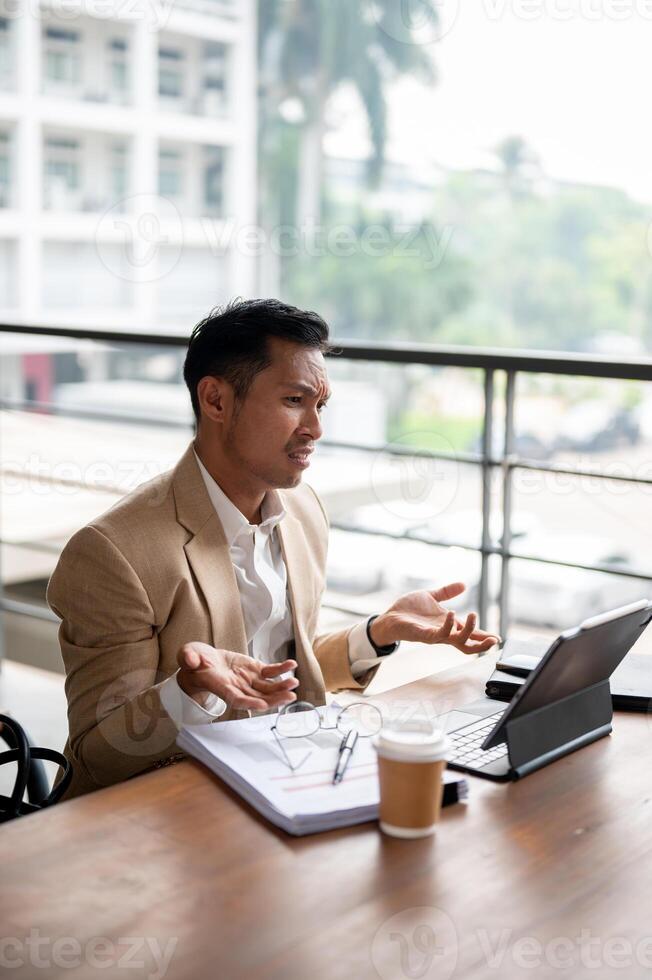 A confused Asian businessman is staring at his digital tablet screen with a puzzled expression. photo