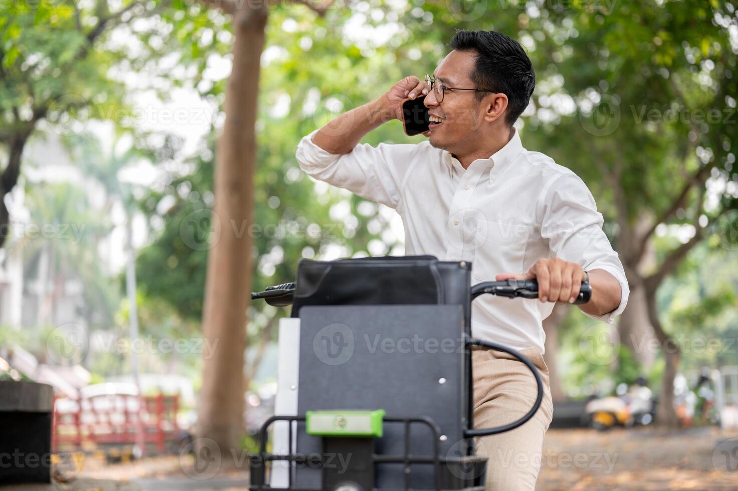 A happy Asian businessman is talking on the phone while he is on a bike, riding a bike to work. photo