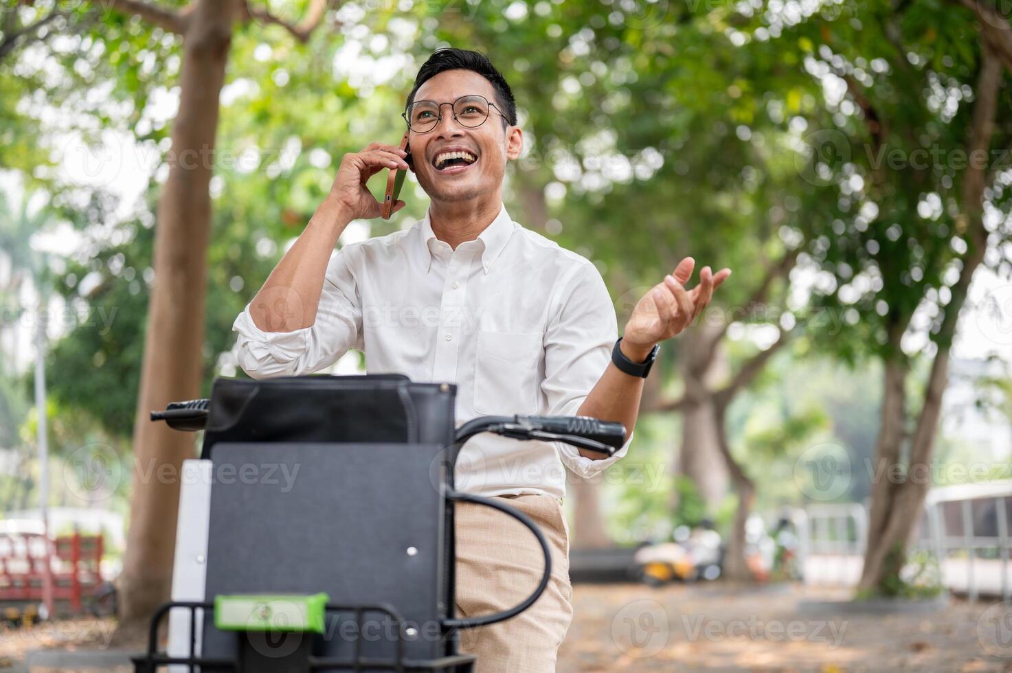 A happy Asian businessman is talking on the phone while he is on a bike, riding a bike to work. photo