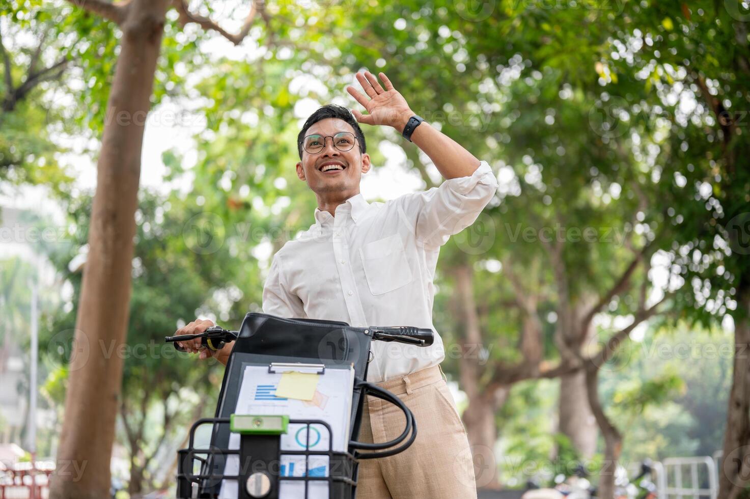 A happy businessman smiles and waves while pushing his bike, greeting someone while heading to work. photo