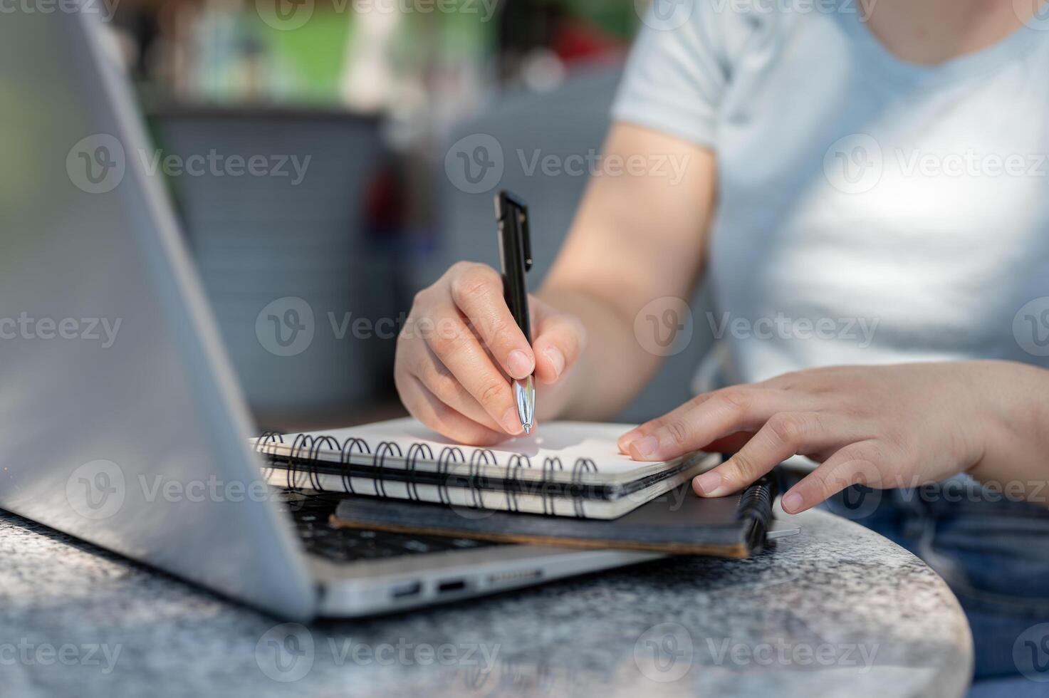 A close-up shot of a woman writing something in her notebook at an outdoor table, working remotely. photo