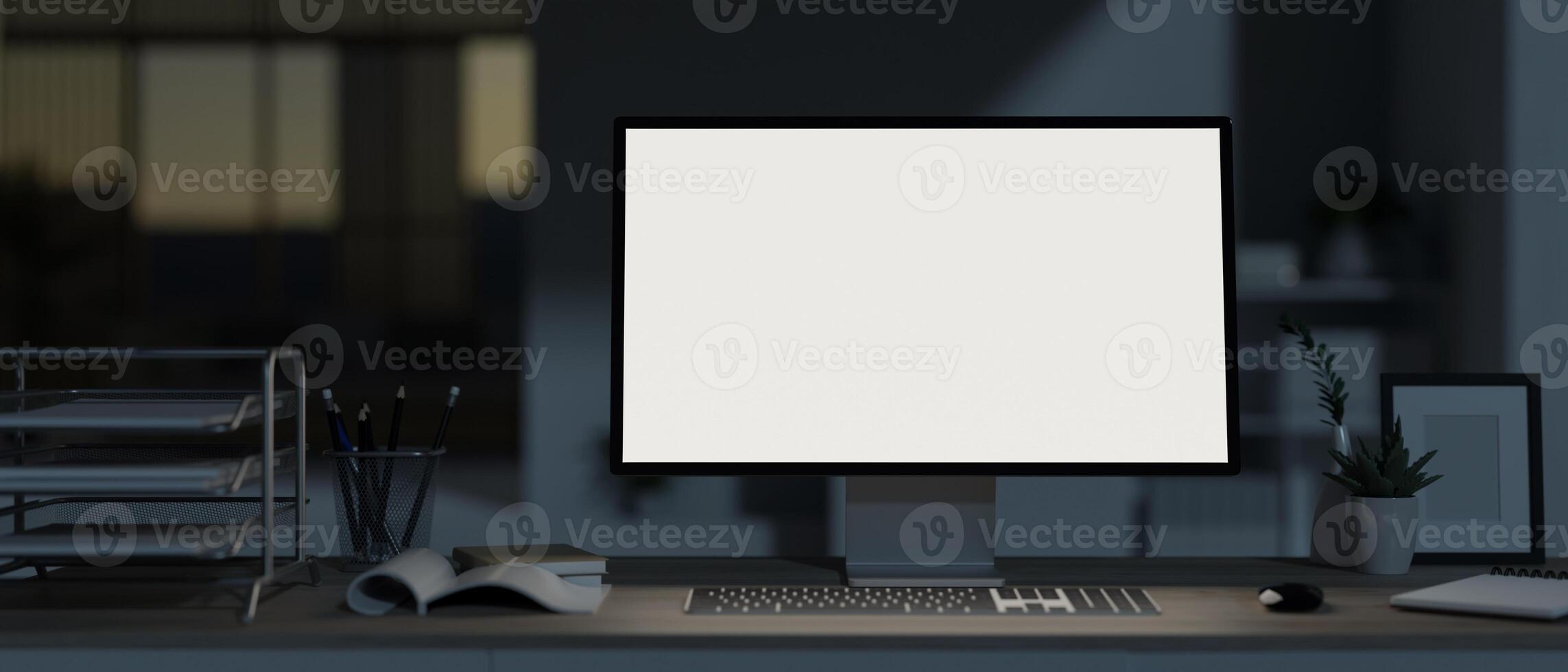 A modern, dark office at night with a white-screen computer mockup and office supplies on the desk. photo