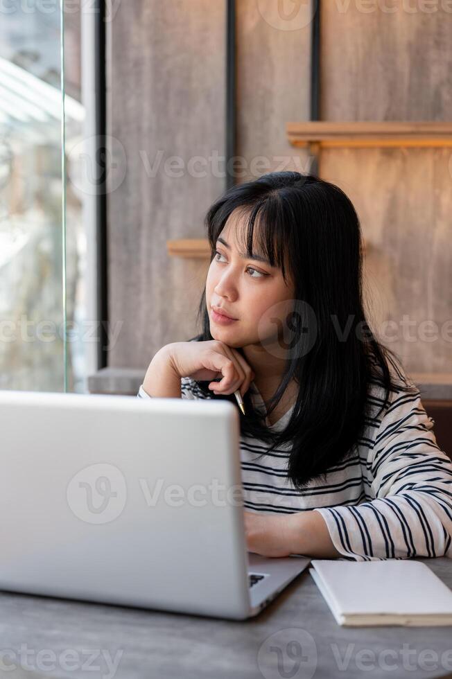 Woman is looking out the window and contemplating something while working remotely at a coffee shop. photo