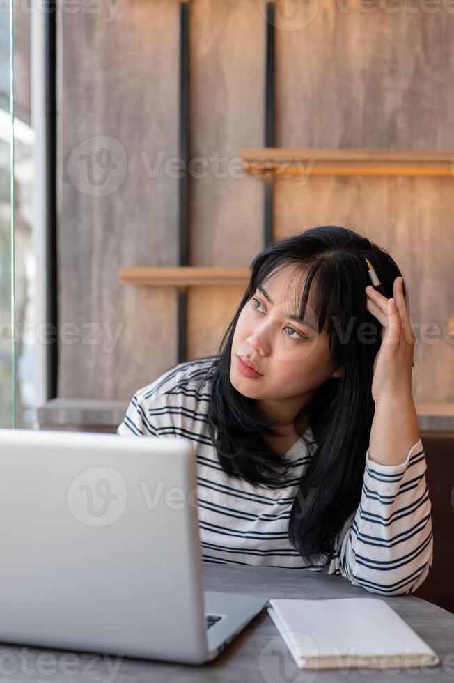 Woman is looking out the window and contemplating something while working remotely at a coffee shop. photo