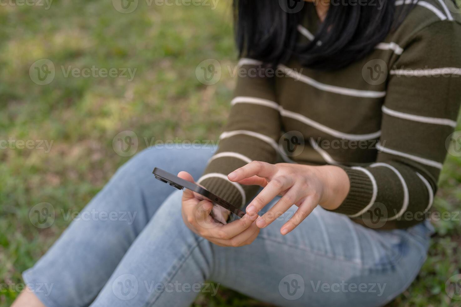 A woman is using her smartphone, chatting with her friends while relaxing in a park. photo