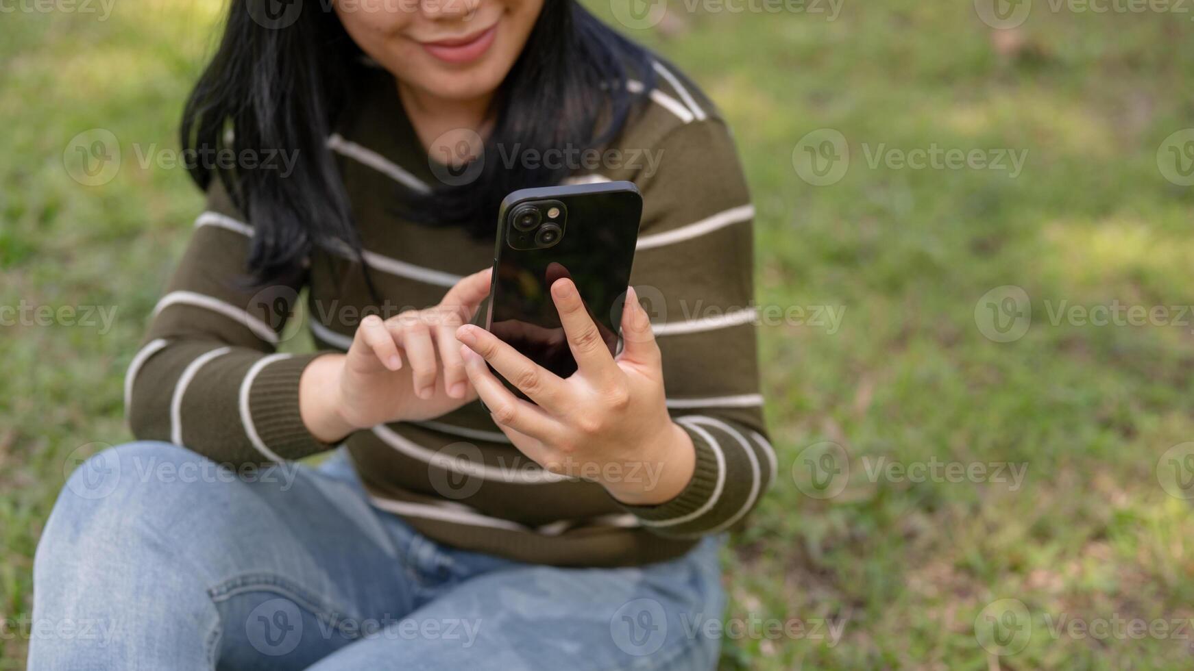 A woman is using her smartphone, chatting with her friends while relaxing in a park. photo