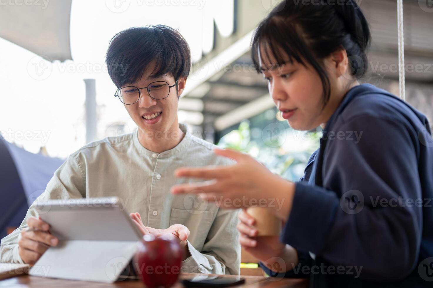 Two young Asian friends or colleagues are discussing and working on a project together at a cafe. photo