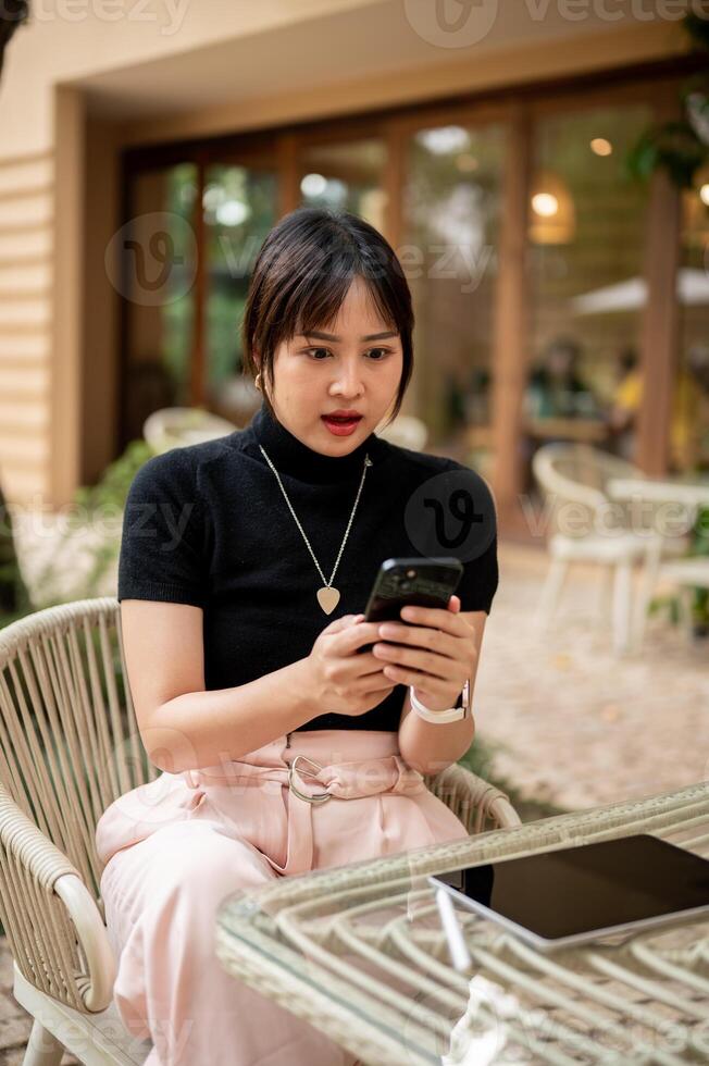 A woman shocked with a message on her phone, sitting at an outdoor table of a cafe. photo