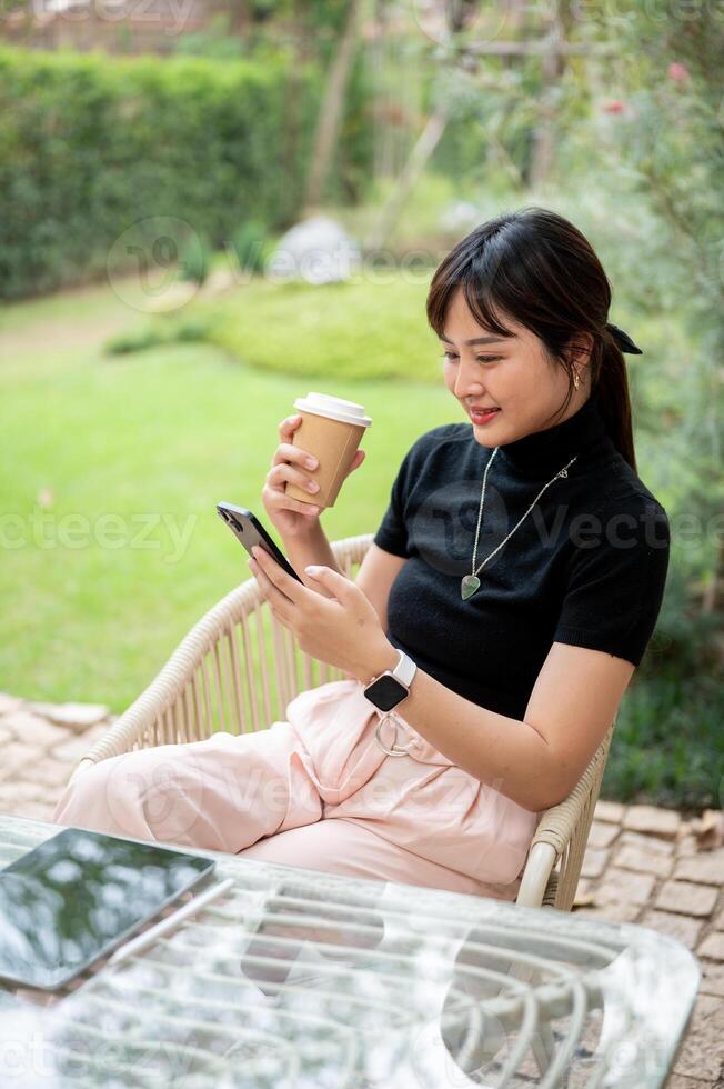 A woman sits at a table in a garden enjoying coffee and chatting with her friend on the phone. photo