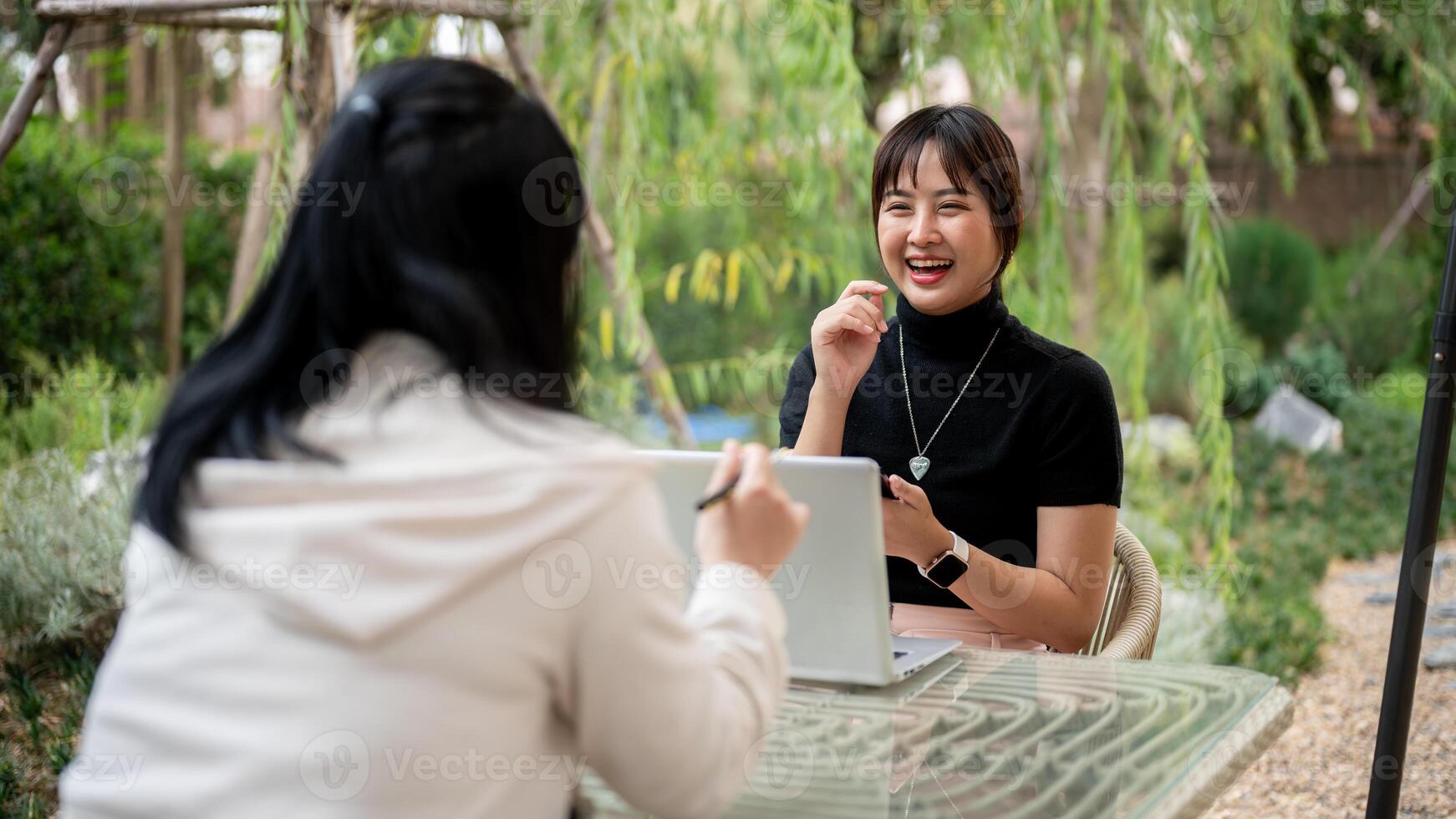 A cheerful Asian woman talking with her friend while working remotely in the garden. photo