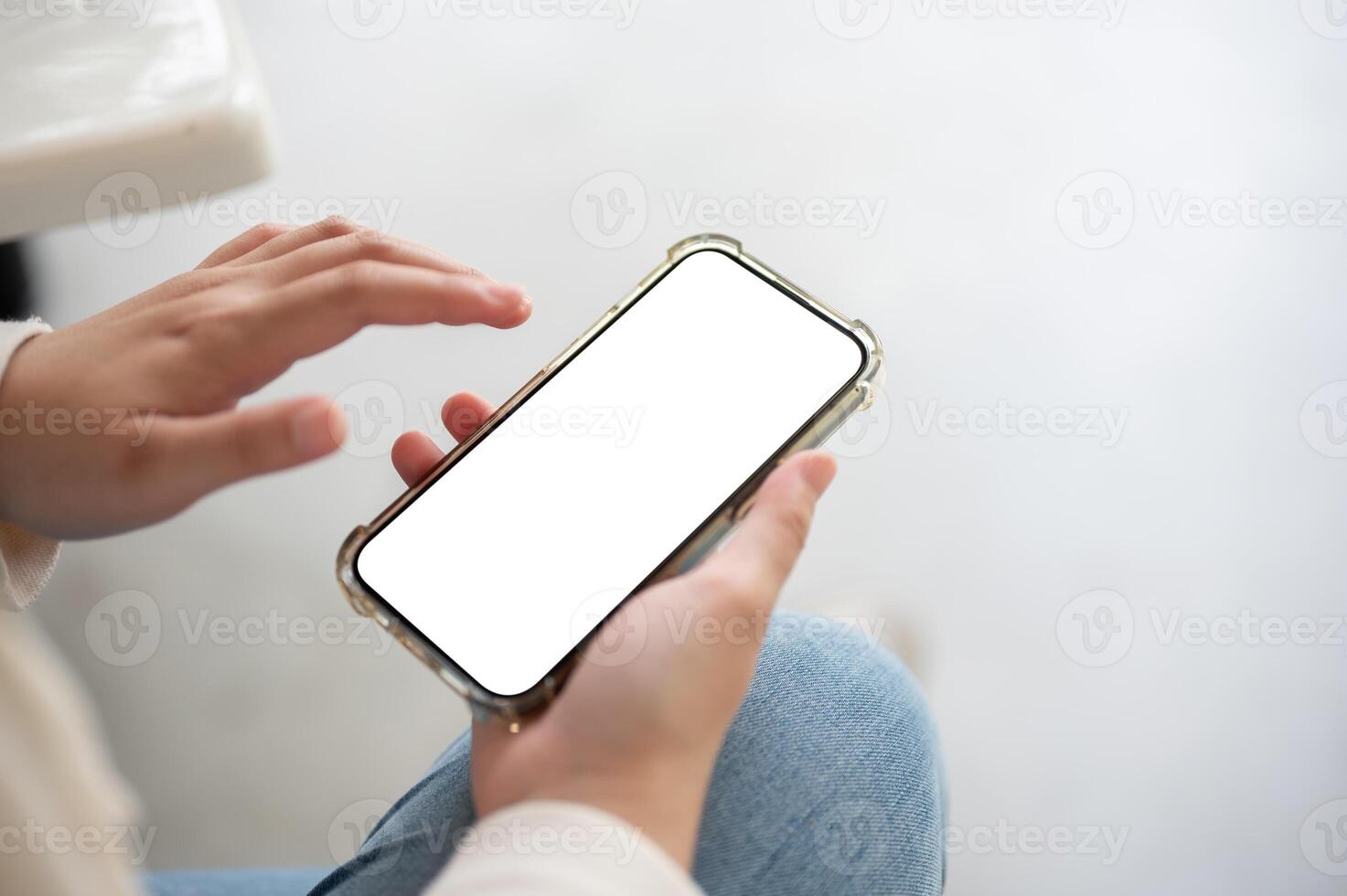 A close-up image of a woman in jeans sits indoor and uses her smartphone. photo