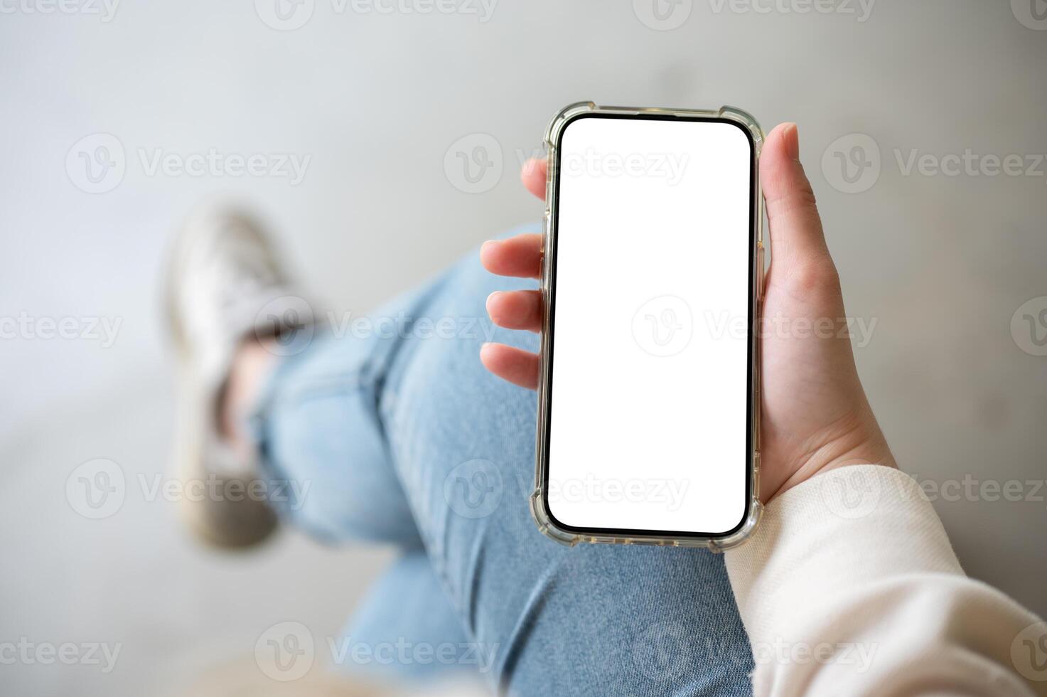 A close-up image of a woman in jeans sits indoor and uses her smartphone. photo
