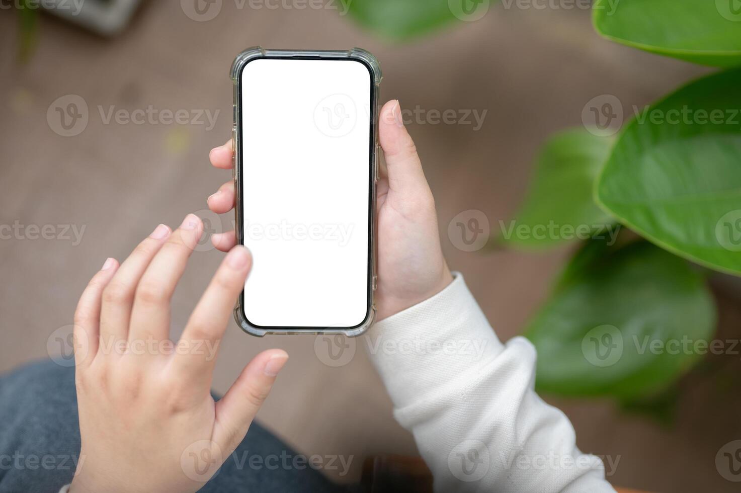 A close-up image of a woman is sitting next to a houseplant indoors and using her smartphone. photo