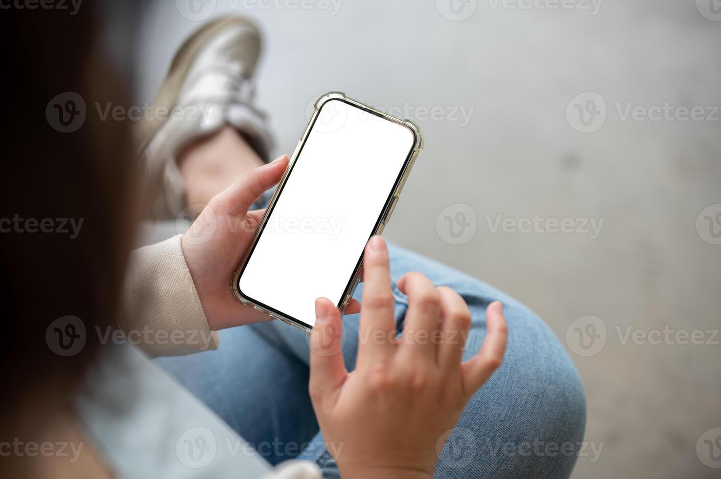 A close-up image of a woman in jeans sits indoor and uses her smartphone. photo