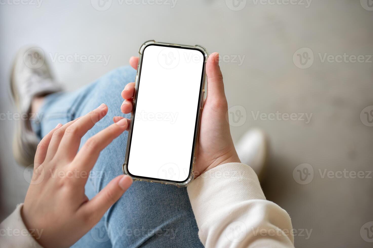 A close-up image of a woman in jeans sits indoor and uses her smartphone. photo