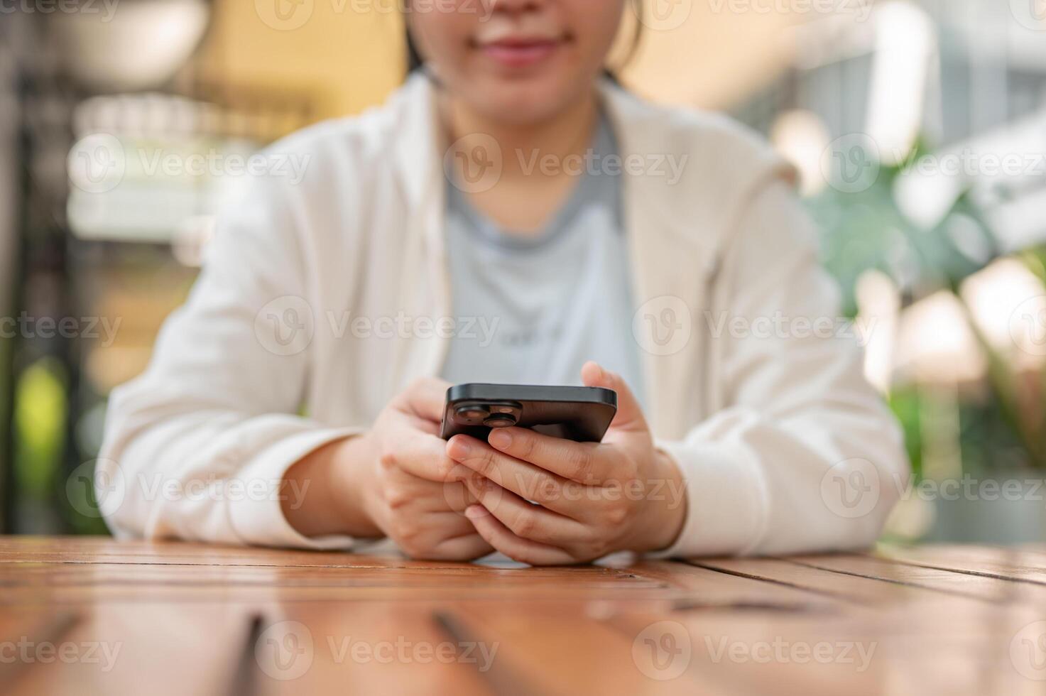 A cropped image of a young positive Asian woman using her smartphone at an outdoor table of a cafe. photo