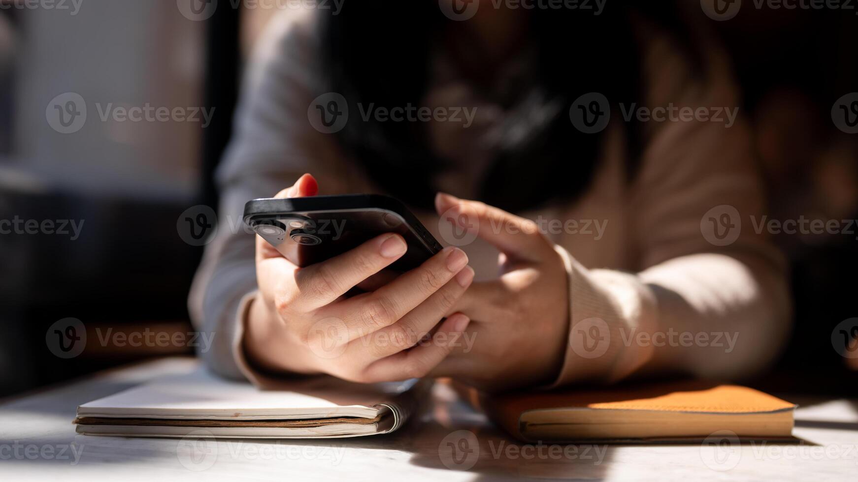 A cropped image of a woman using her smartphone at a table by the window on a sunny day. photo