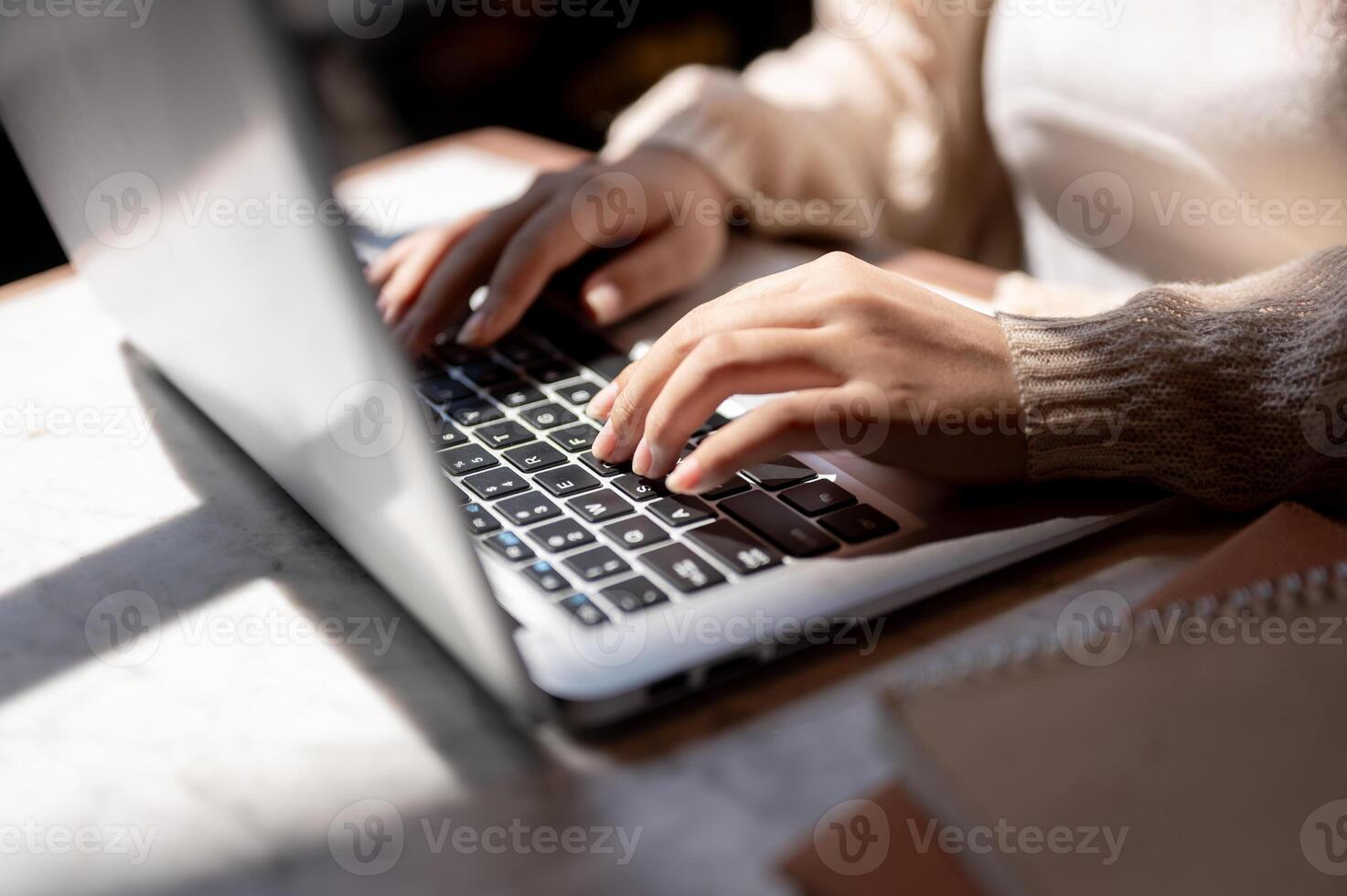 Close-up image of a woman typing on keyboard, working on her laptop computer at a table indoors. photo