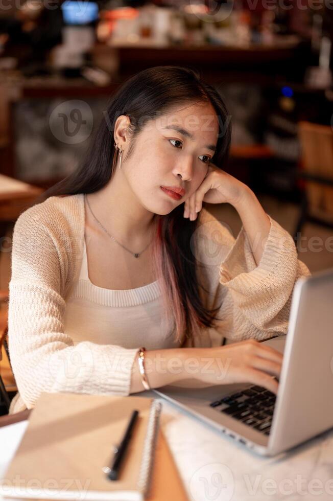 Young bored and tired Asian woman working on her laptop computer at a coffee shop, lack of energy. photo