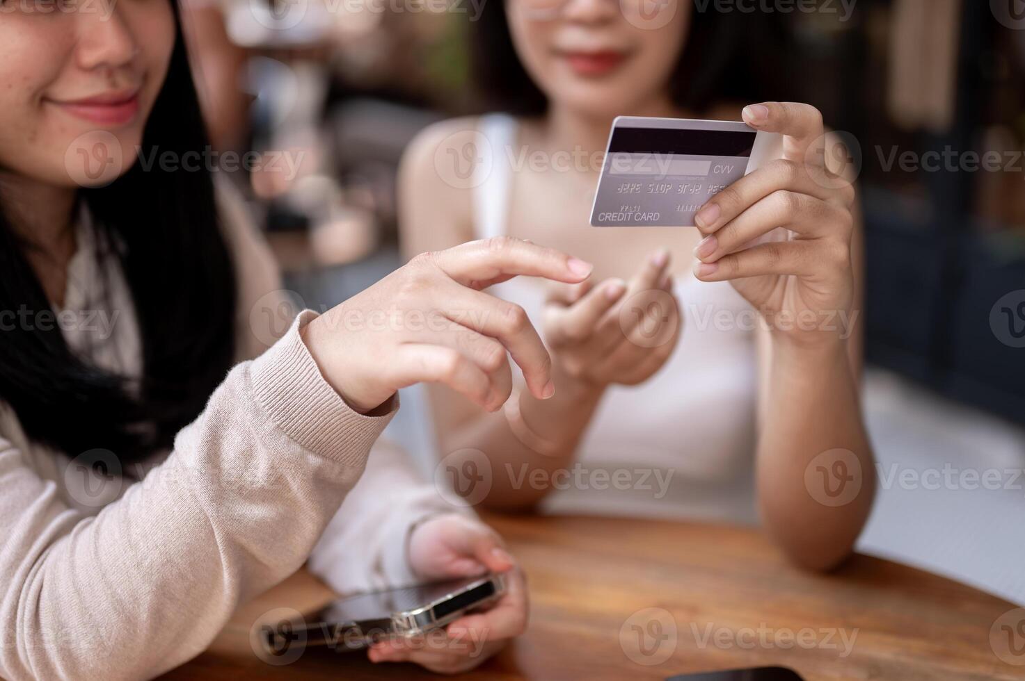 Two happy Asian female friends are talking about the benefits of their credit cards at a cafe. photo