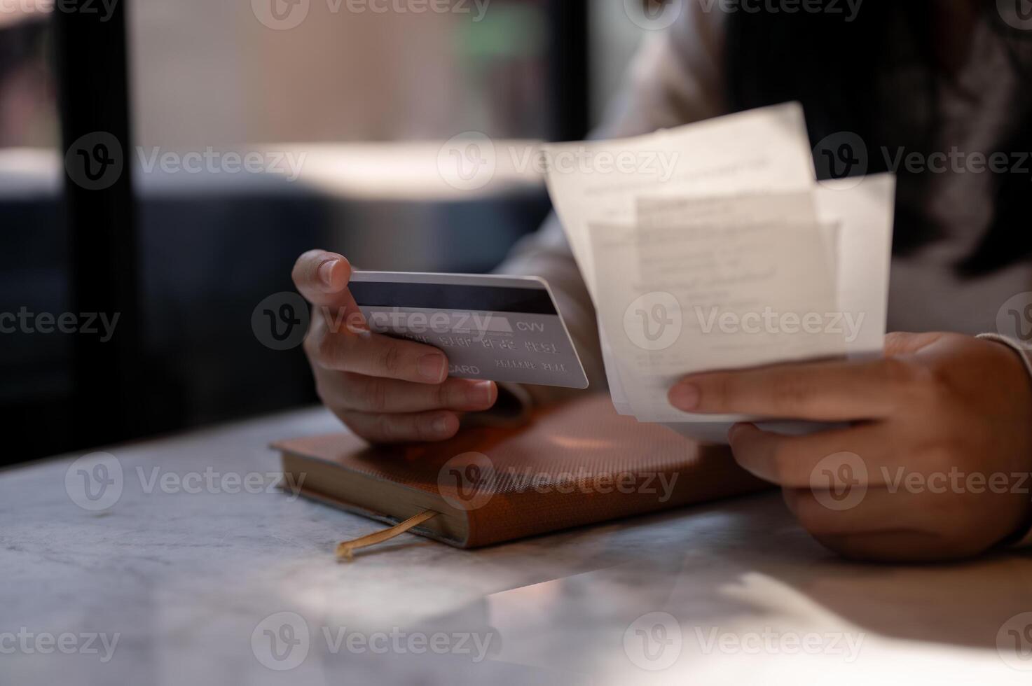 A cropped image of a woman holding her credit card and receipt, sitting at a table indoors. photo