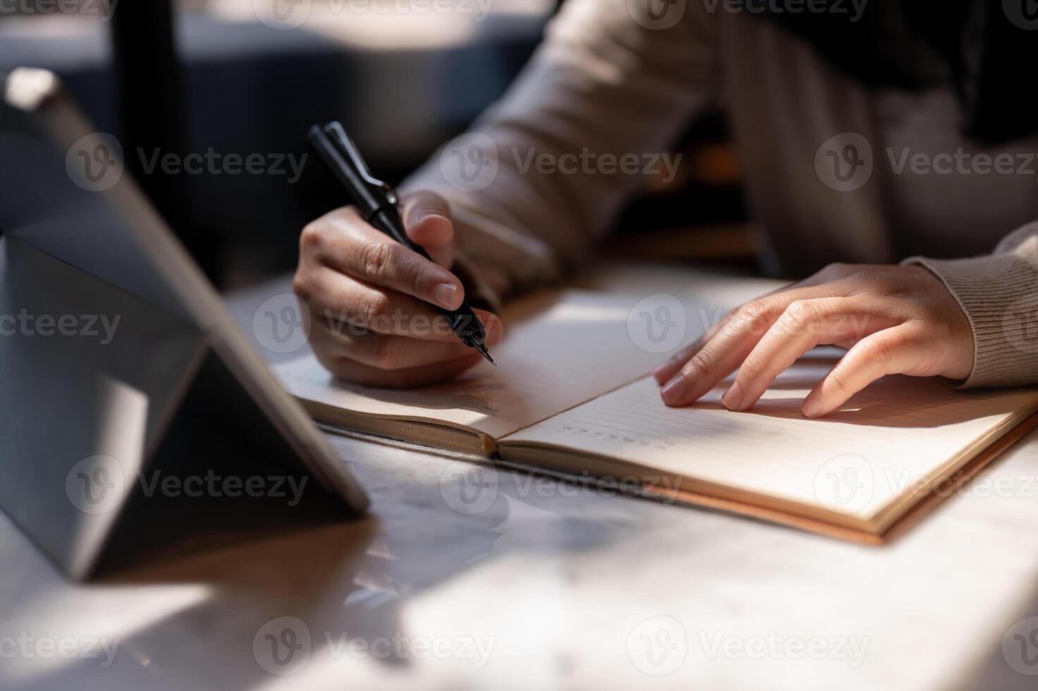 A cropped image of a female college student taking notes while studying online on her tablet. photo