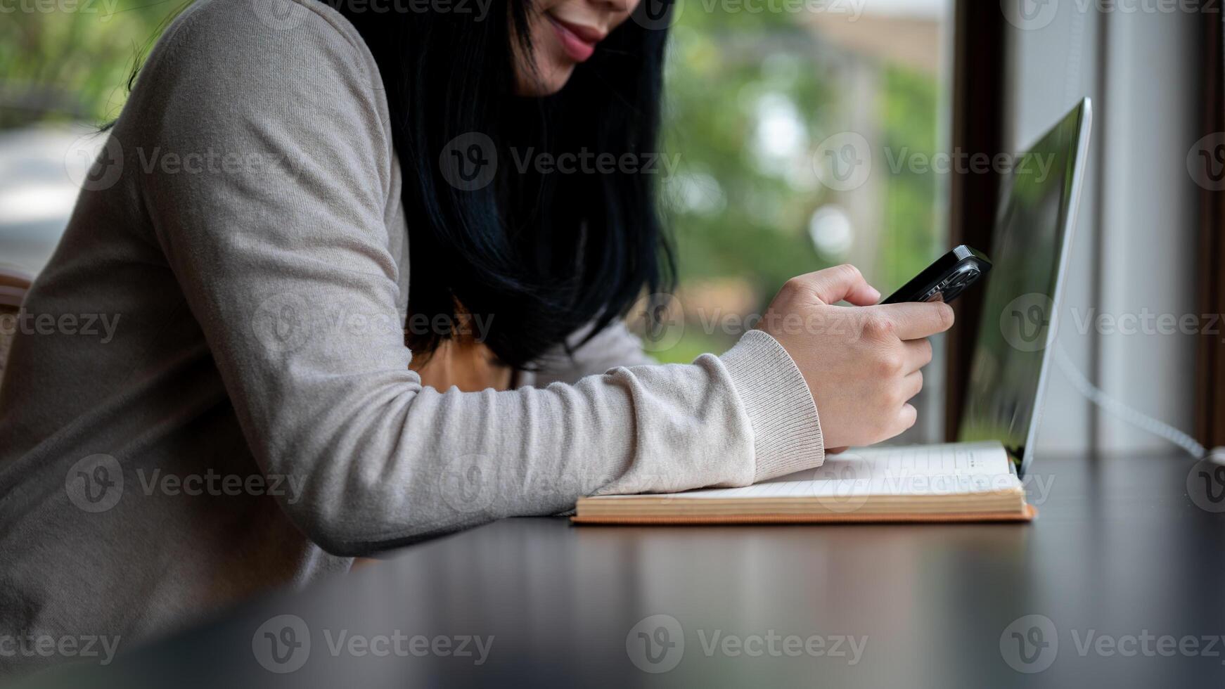 A cropped side view image of an Asian woman using her smartphone while sitting in a coffee shop. photo