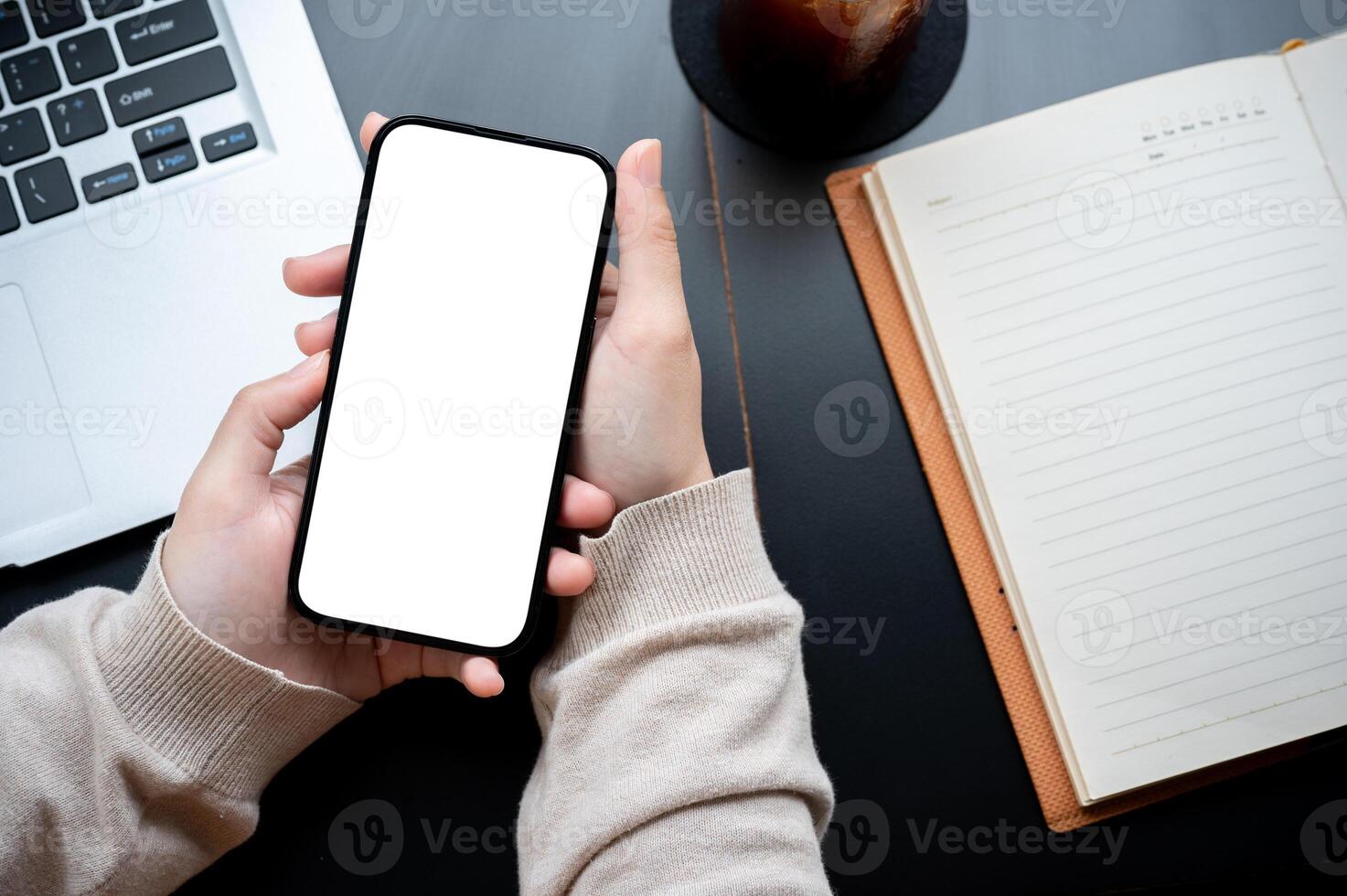 Top view image of a woman's hand holding a white-screen smartphone mockup over a modern office desk. photo