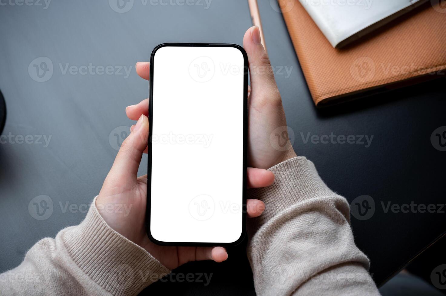 Top view image of a woman's hand holding a white-screen smartphone mockup over a modern office desk. photo