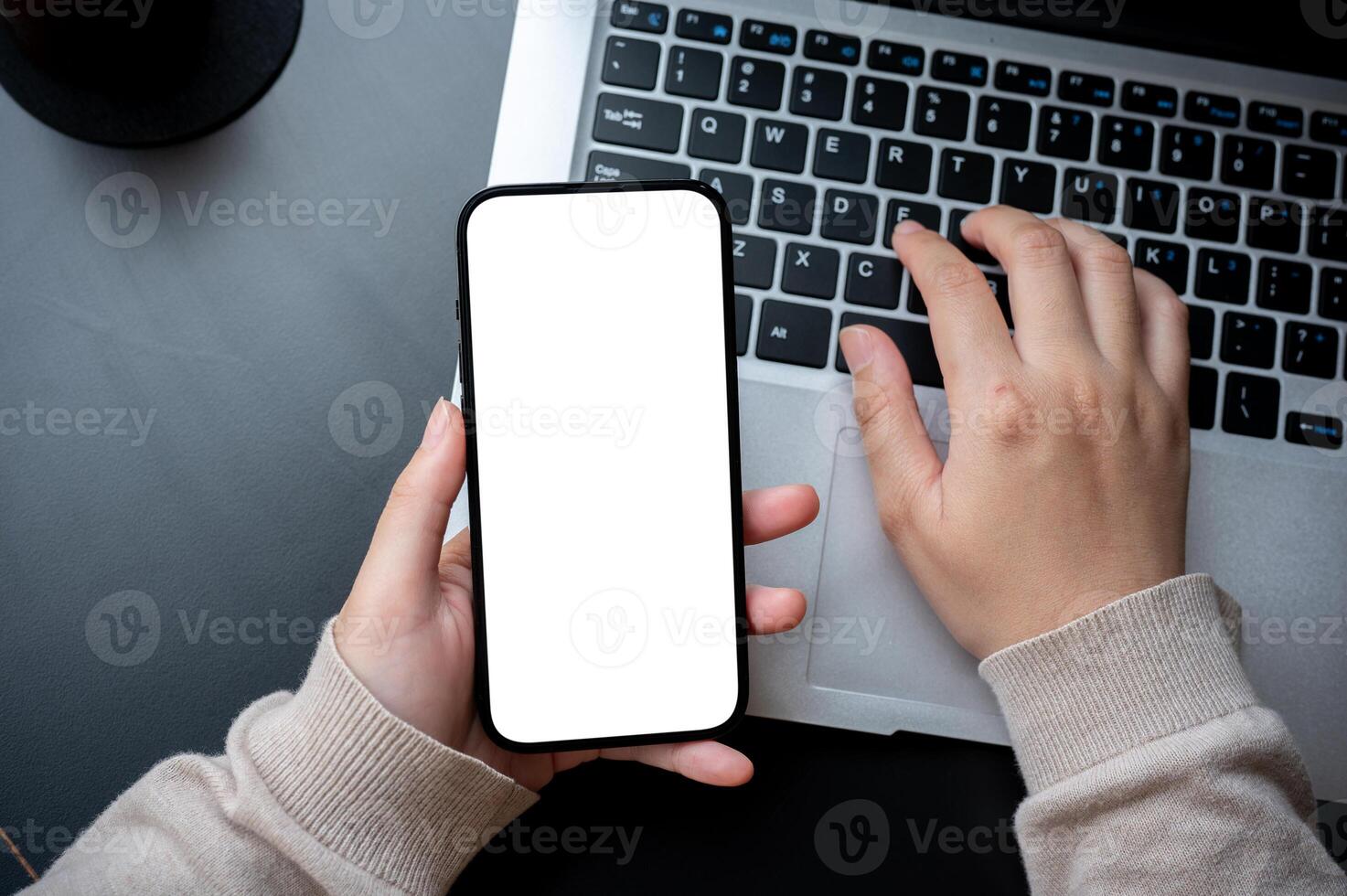 A top view image of a woman typing on laptop keyboard and holding a white-screen smartphone mockup. photo