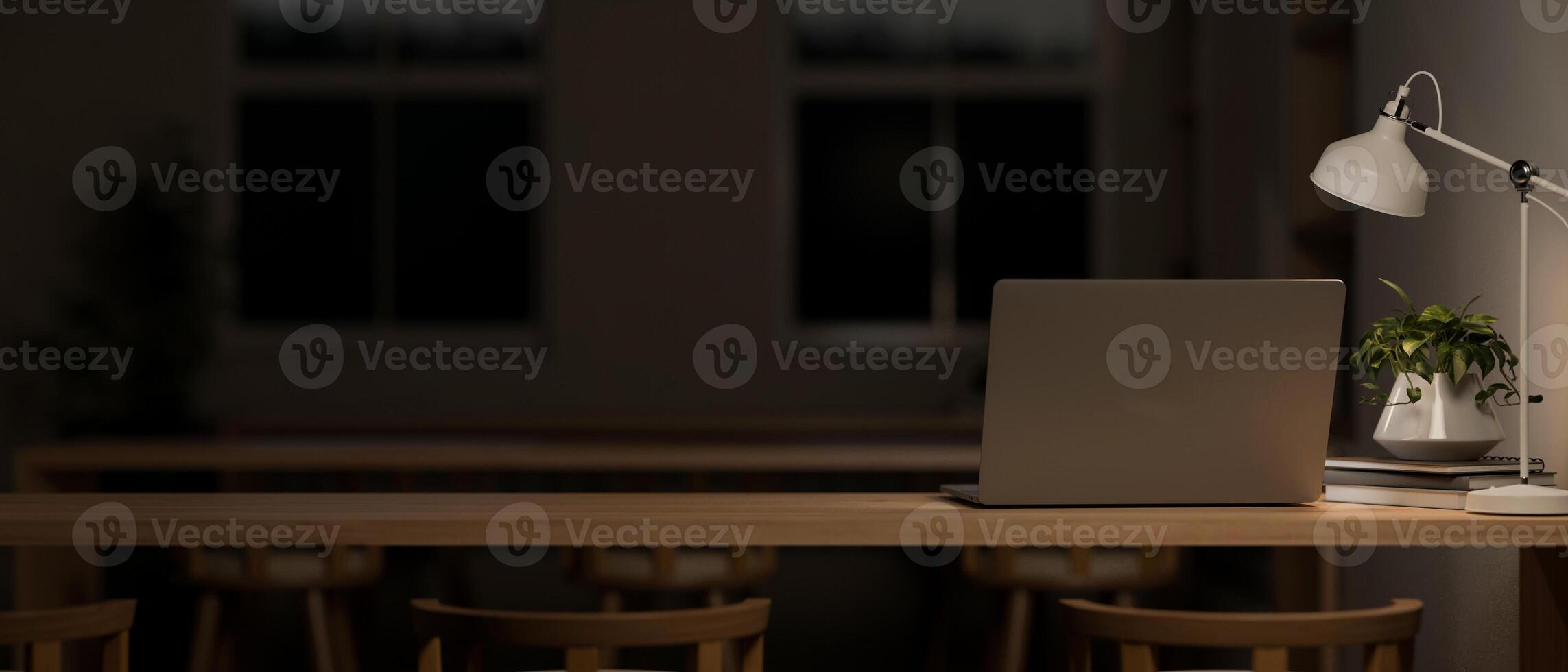 A dark classroom or co-working space at night features a laptop computer on a wooden table. photo
