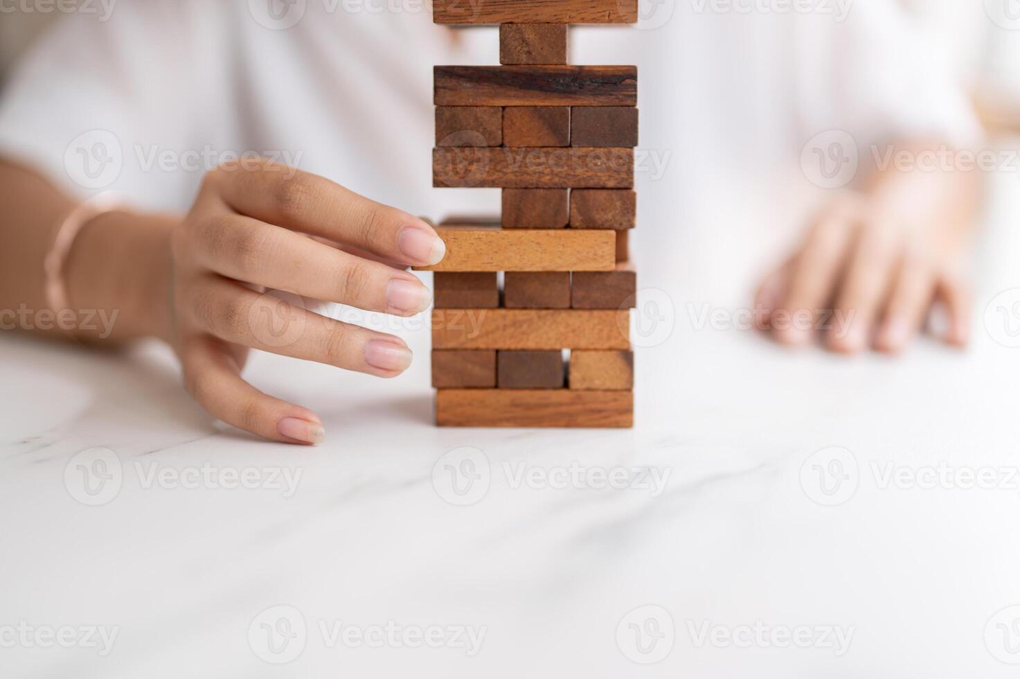 A woman pays her attention on playing a wooden block game at a table, moving a wooden block. photo