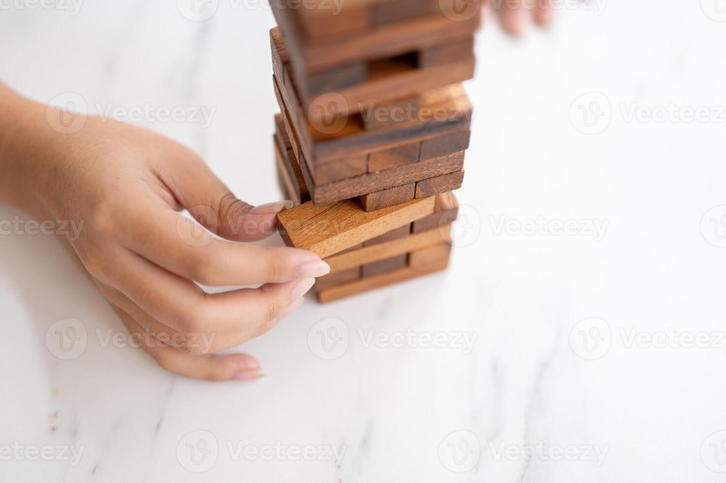 A woman pays her attention on playing a wooden block game at a table, moving a wooden block. photo