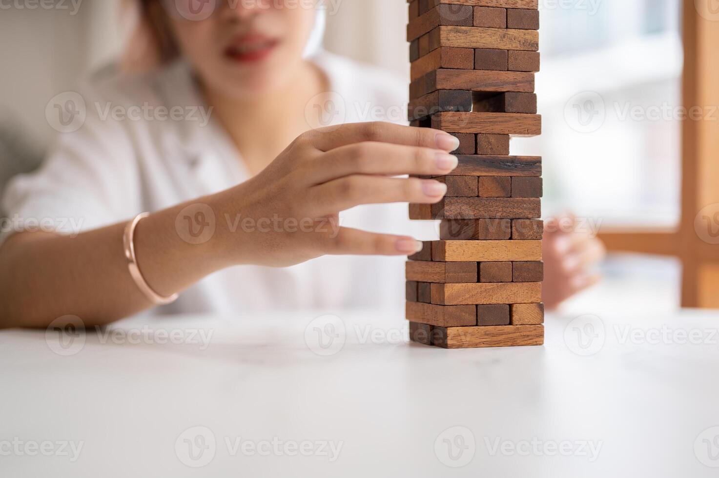 A woman pays her attention on playing a wooden block game at a table, moving a wooden block. photo
