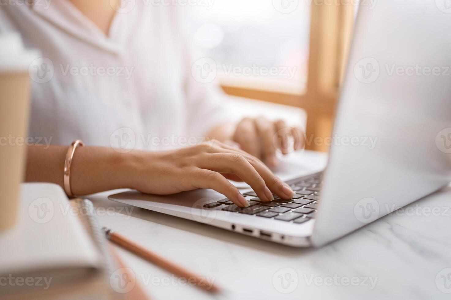 A close-up image of a woman typing on keyboard, working on the computer at a table in a coffee shop. photo