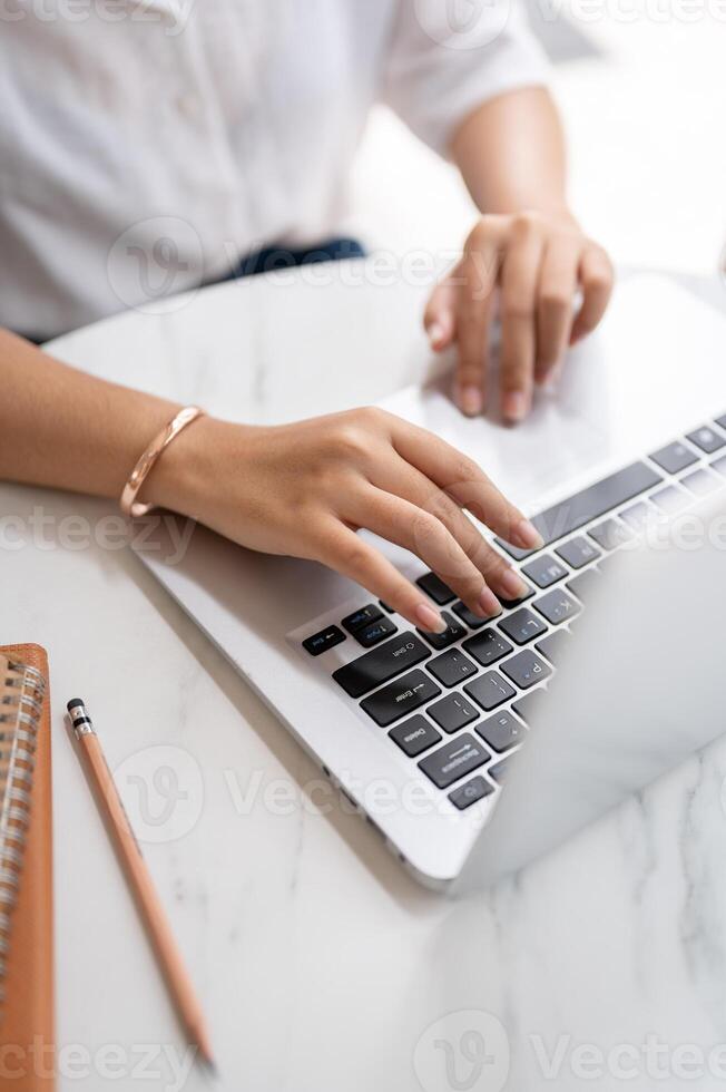 A close-up image of a woman typing on keyboard, working on the computer at a table in a coffee shop. photo