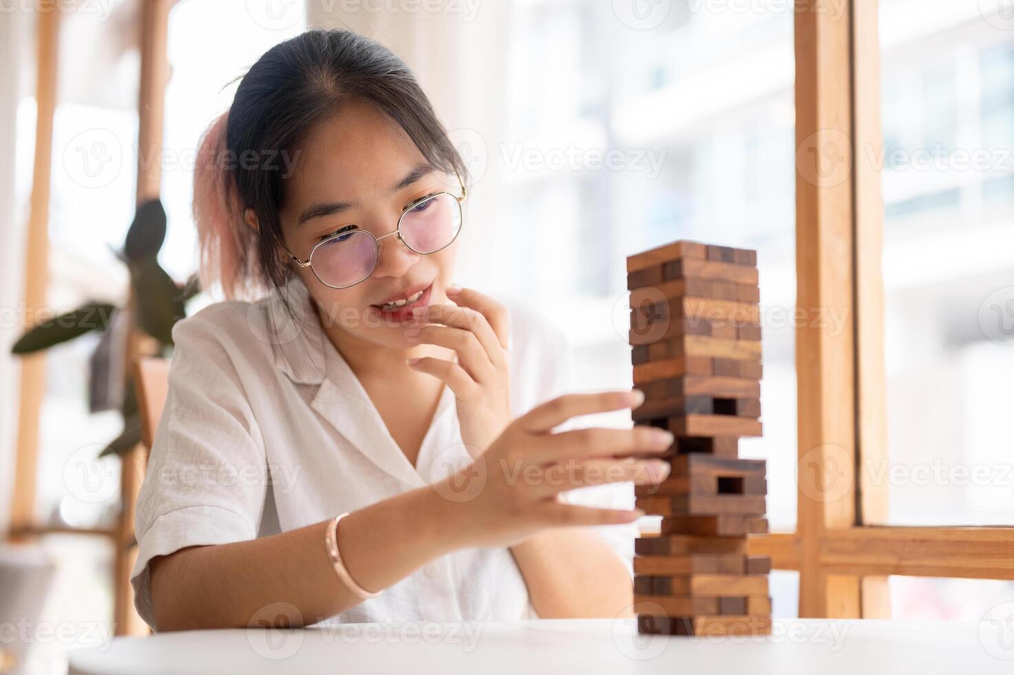 A young Asian woman focusing on playing a wooden block game at a table indoors. photo