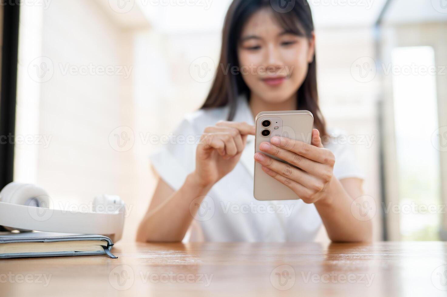 A beautiful, happy Asian woman using her smartphone while sitting in a cafe or co-working space. photo