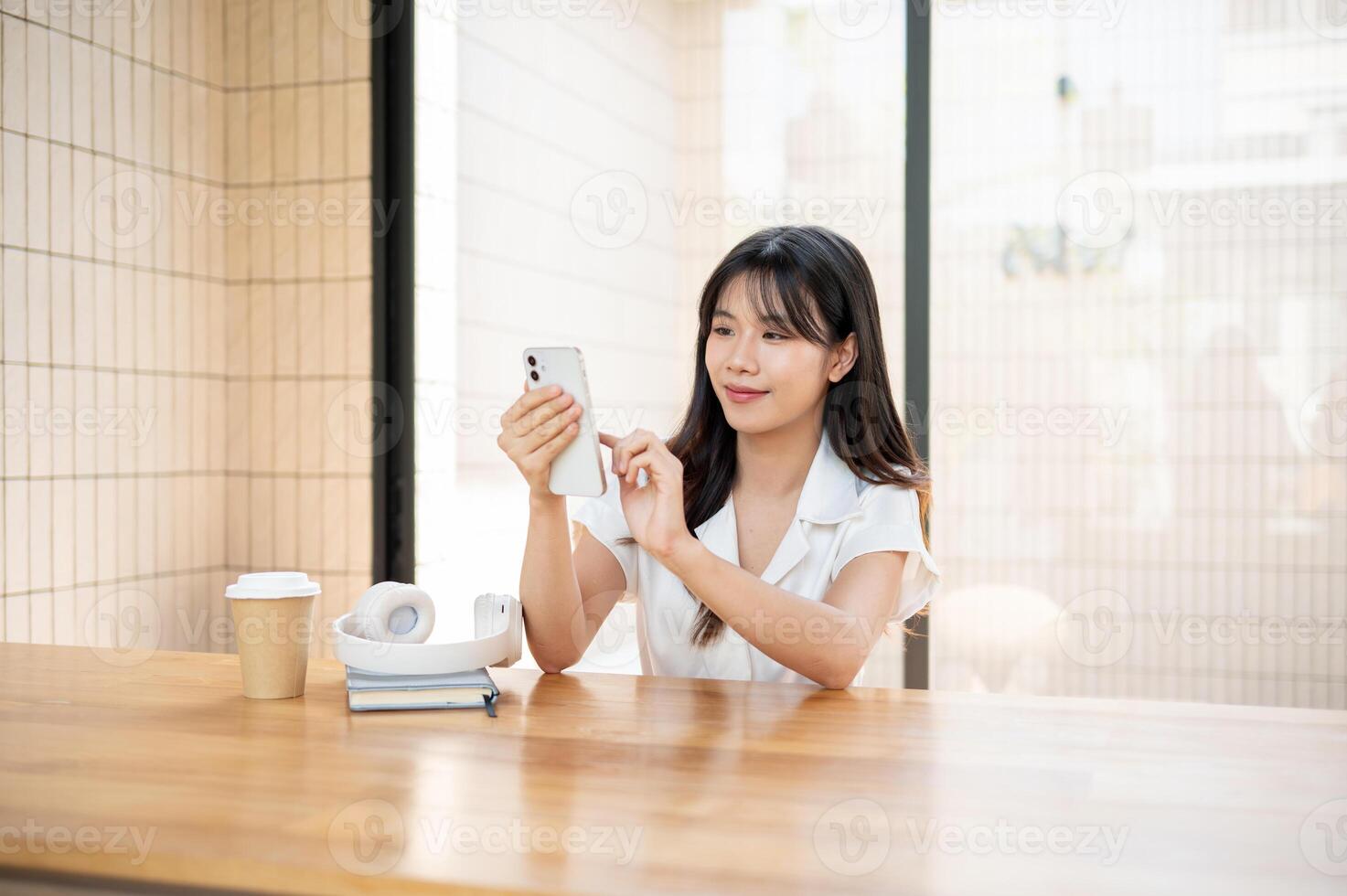 A beautiful, happy Asian woman using her smartphone while sitting in a cafe or co-working space. photo