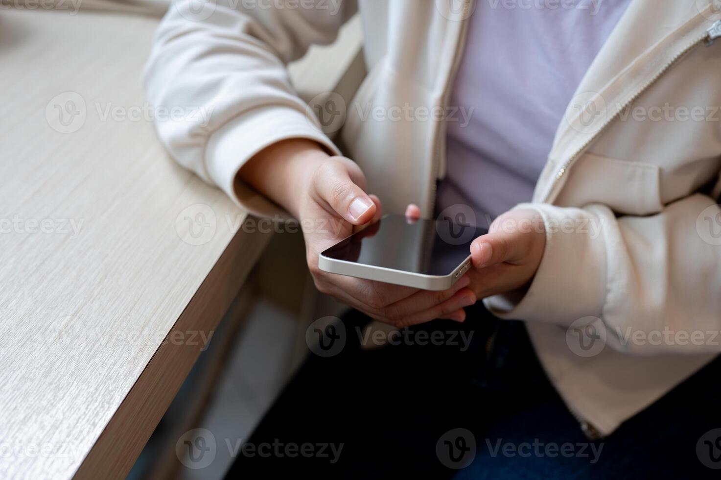 A close-up image of a woman in casual wear using her smartphone at a table indoors. photo