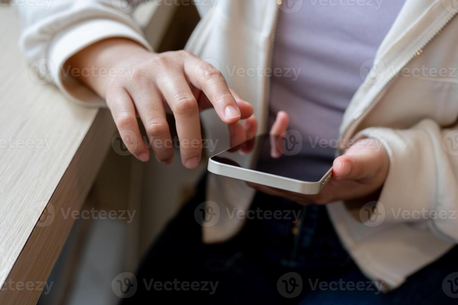 A close-up image of a woman in casual wear using her smartphone at a table indoors. photo