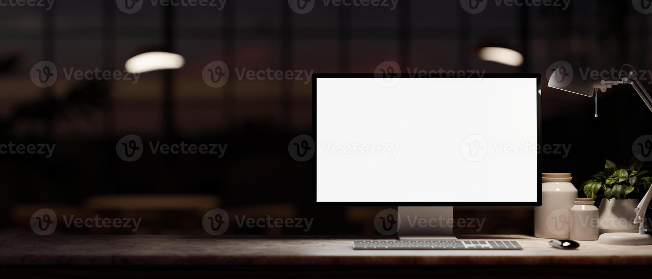 A computer mockup, decor, and a dim light from a lamp on a table in a dark office room at night. photo