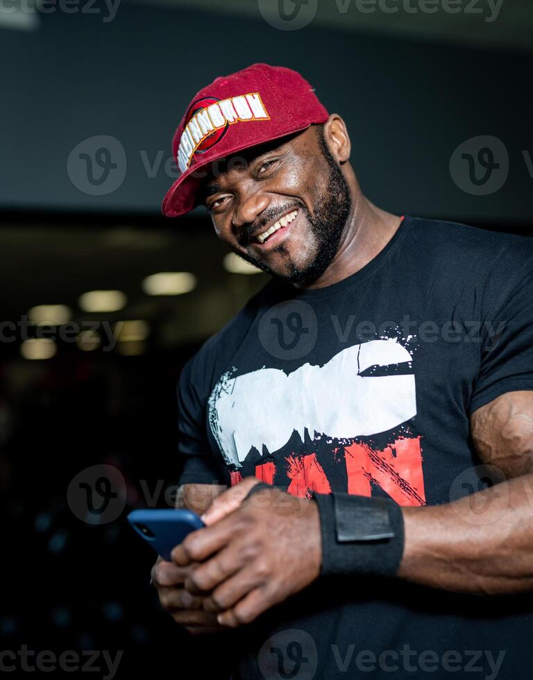 Attractive handsome man in cap smilling in gym. Muscular strong male resting in the gym. photo
